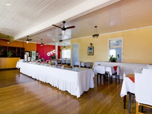 A spacious dining area with a long buffet table, ceiling fans, and a yellow wall with a red section. - OYO Imperial Parque Hotel (Nova Petropolis)
