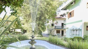 Un patio con una fuente, rodeado de follaje y un edificio con múltiples ventanas y balcones.