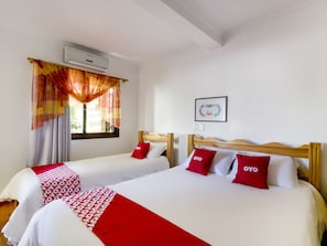 A hotel room with two beds, each with a red and white bedspread and matching pillows. There is an air conditioning unit on the wall, a window with curtains, and a framed picture on the wall. - OYO Imperial Parque Hotel (Nova Petropolis)