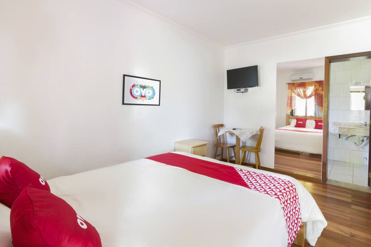 Ein Hotelzimmer mit Bett, Schreibtisch, Stuhl, Fernseher und einem Badezimmer mit Dusche und Spiegel.