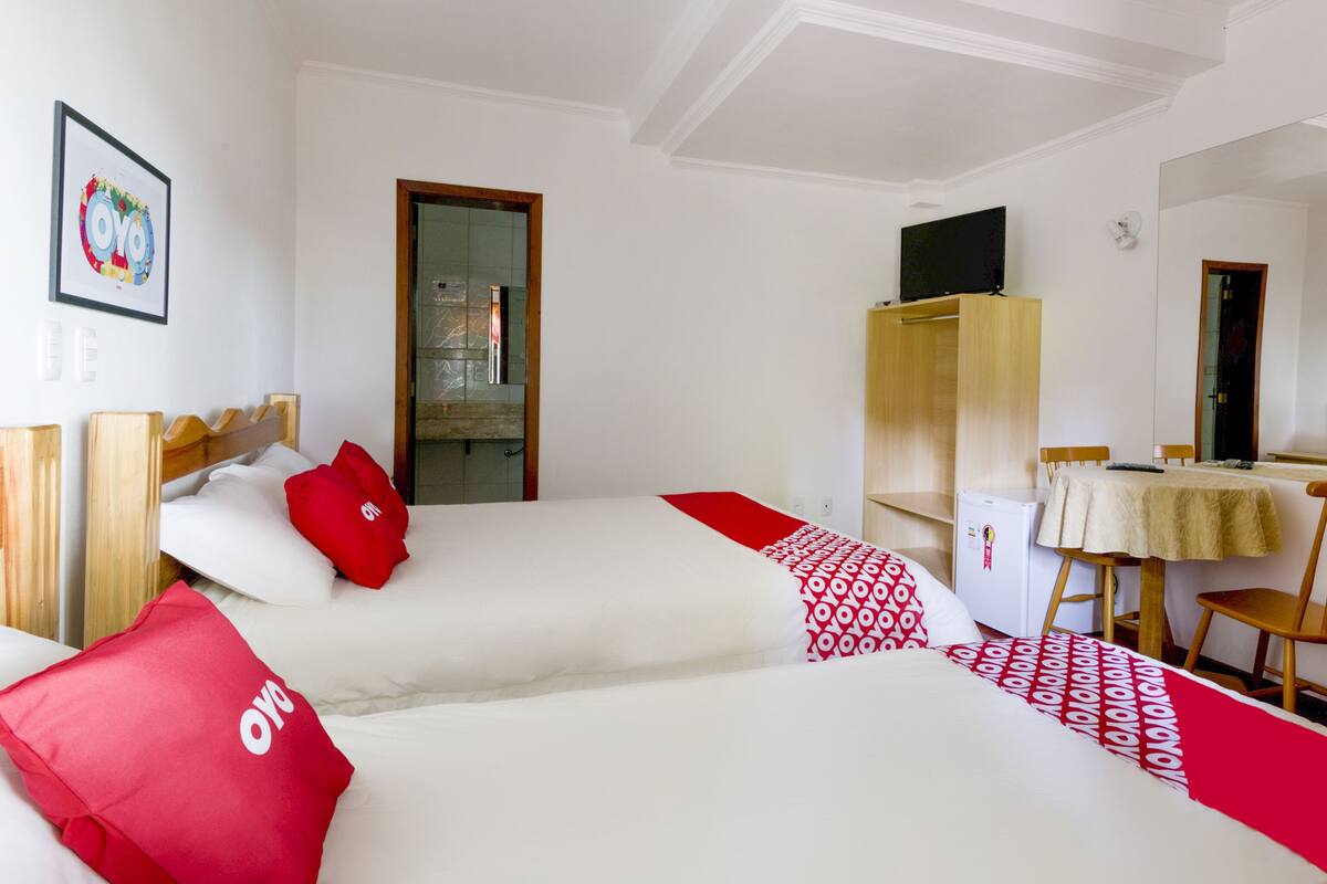 Ein Hotelzimmer mit zwei Betten, einem Schreibtisch, einem Stuhl, einem Kleiderschrank und einem Fernseher.
