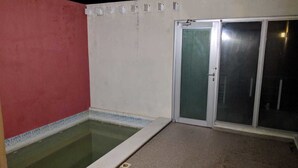 A small outdoor pool area with a red wall and a glass door leading to a covered space.