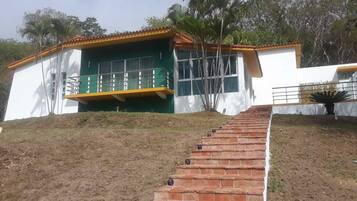Un edificio de dos plantas con fachada verde y blanca, un balcón y una escalera de ladrillo que conduce a la entrada.