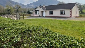 A single-story house with a sloped roof, a front porch, and a stone wall in the background.