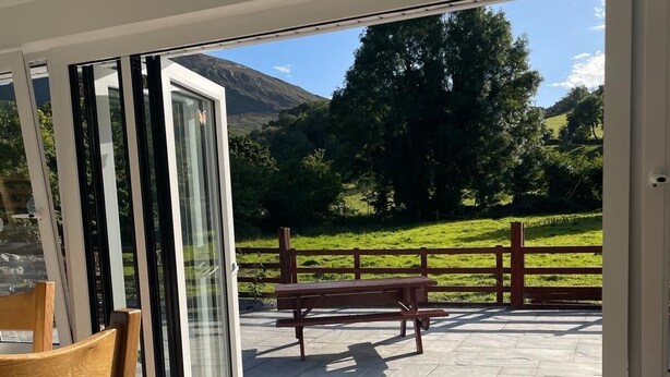 A patio area with a wooden bench and a table, a glass door leading to a scenic outdoor view.