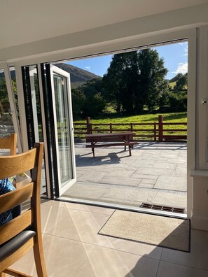 A patio area with a wooden bench and a table, a glass door leading to a scenic outdoor view.