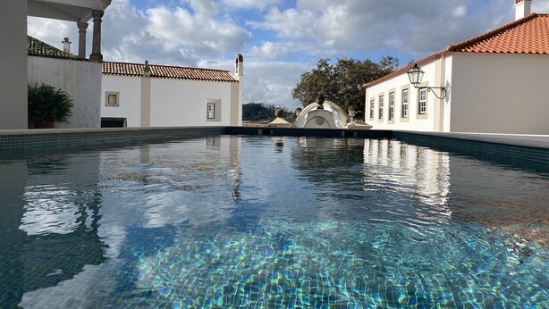 Una piscina cristalina con un borde empinado de baldosas, rodeada de edificios blancos con tejados rojos y un cielo despejado.
