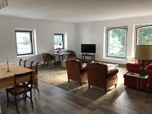 A spacious living room with a dining area, large windows, a flat-screen TV, and a red sofa.
