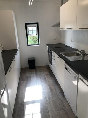 A compact kitchen with white cabinets, a black countertop, and a window providing natural light.