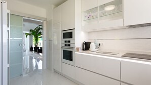 A modern kitchen with white cabinetry, a glass backsplash, and stainless steel appliances. - A unique house in a fabulous position near  Galé beach (Gale)
