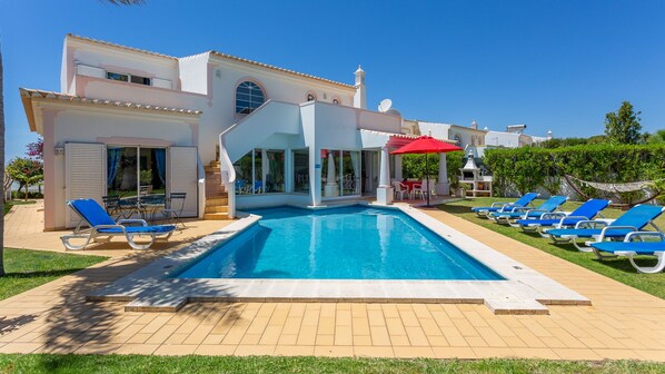 Une villa moderne dotée d’une piscine, de chaises longues et d’un patio couvert.