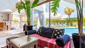 A modern living room with a glass table, a sofa with patterned cushions, and large potted plants. - A unique house in a fabulous position near  Galé beach (Gale)