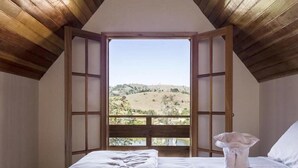 Un dormitorio con un ventanal grande, una cama con edredón blanco y techo de madera.