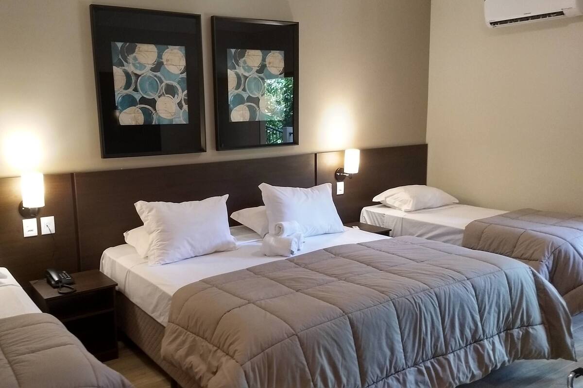 A hotel room with two beds, a nightstand, a telephone, and artwork on the wall.