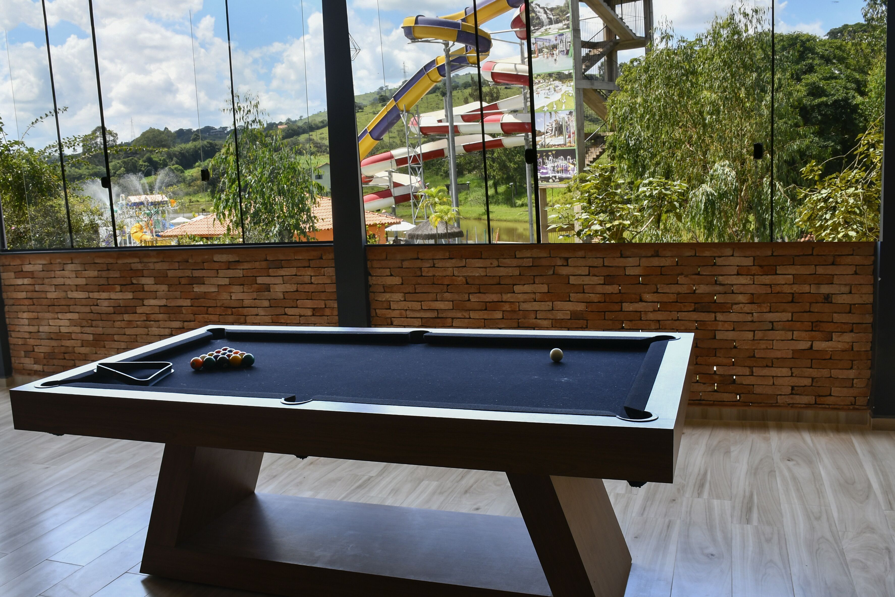 A pool table in a room with a brick wall and large windows overlooking a water park.