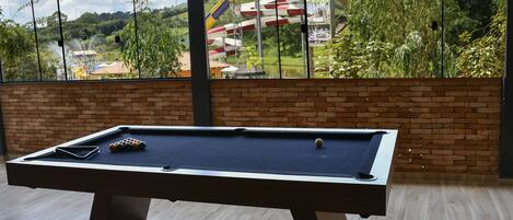 A pool table in a room with a brick wall and large windows overlooking a water park.