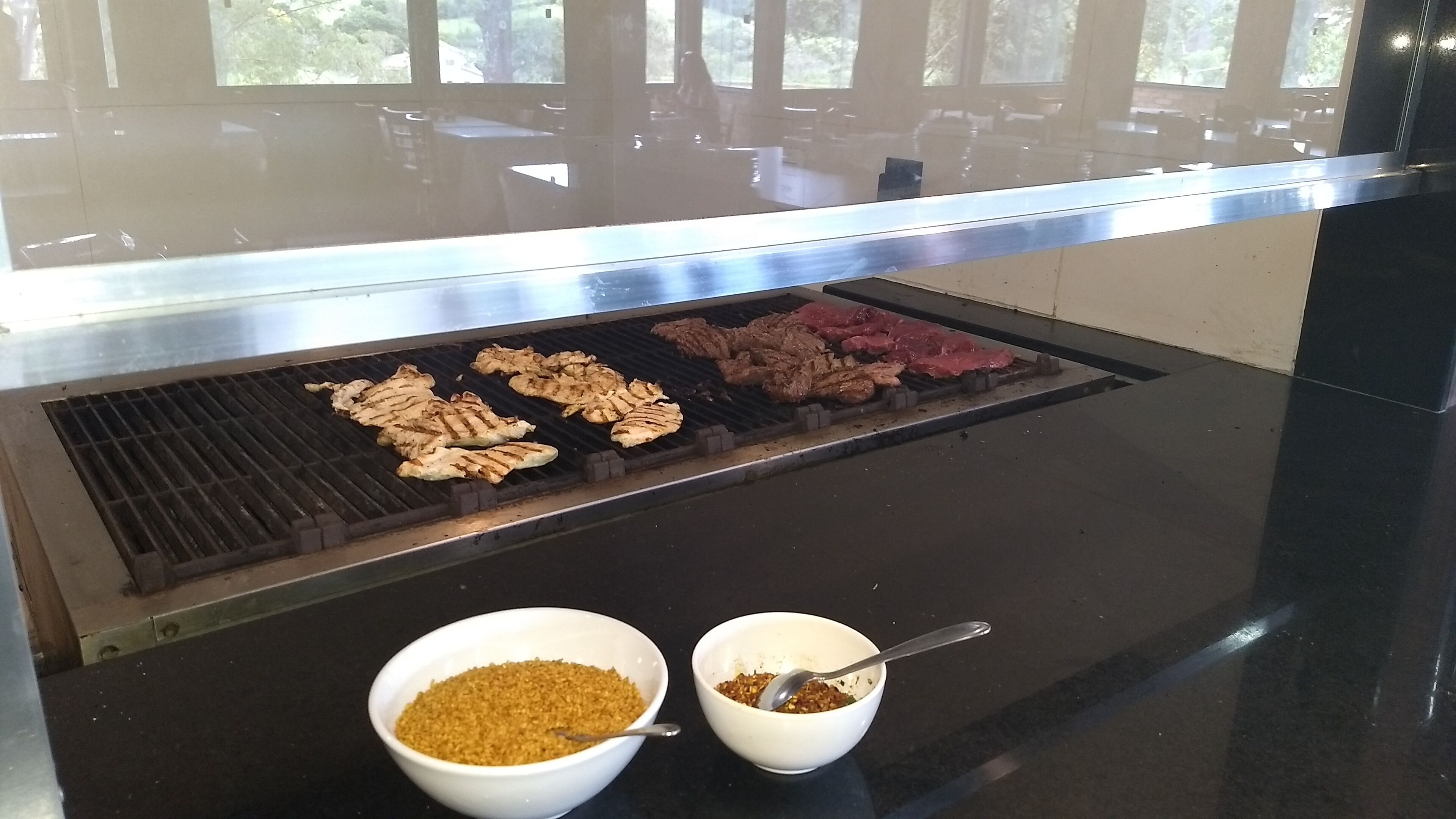 Ein Grill mit verschiedenen Fleisch- und Gemüsesorten, die zubereitet werden. Es befinden sich zwei Schalen mit Gewürzen oder Beilagen darauf.