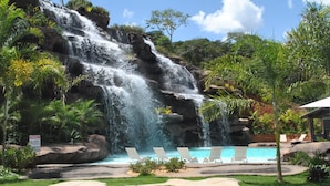 Zona de piscina con cascada, sillas de descanso y un cartel que indica área restringida.