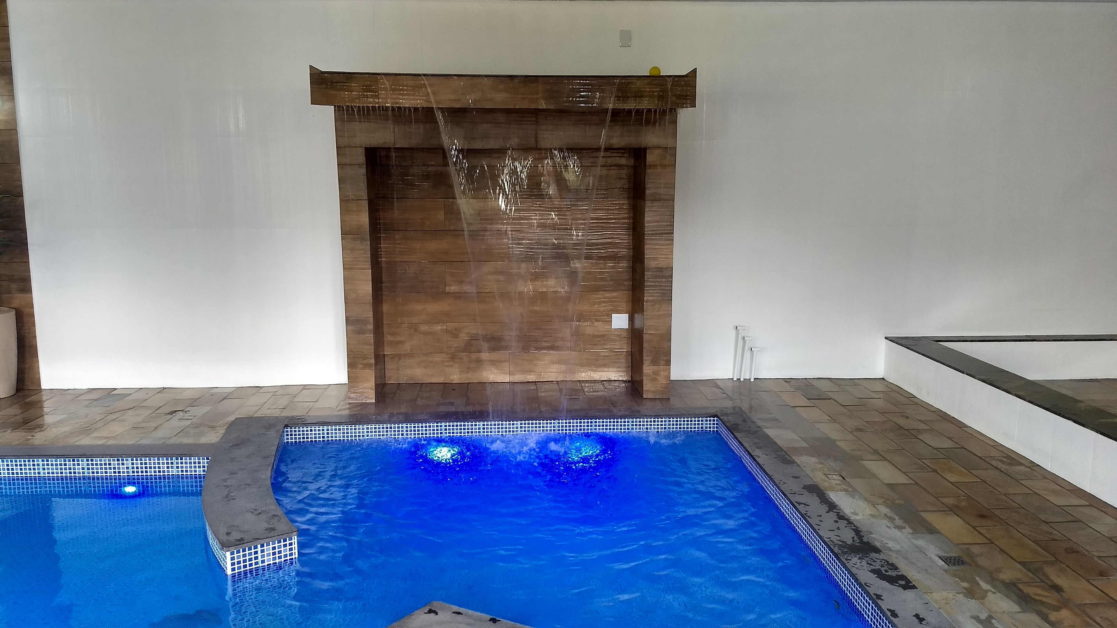 Une piscine agrémentée d’un élément décoratif aquatique en bois et dotée d’un revêtement de sol carrelé.