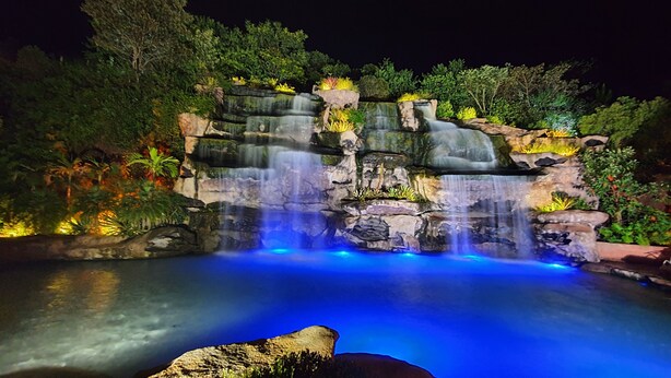 Una cascada iluminada de noche, con plantas y una piscina cristalina en la base.