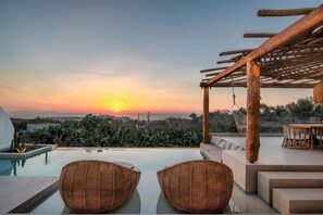 Un espace piscine aménagé sur le toit, avec des fauteuils en osier, une pergola en bois et une vue imprenable sur le coucher de soleil et le paysage environnant.