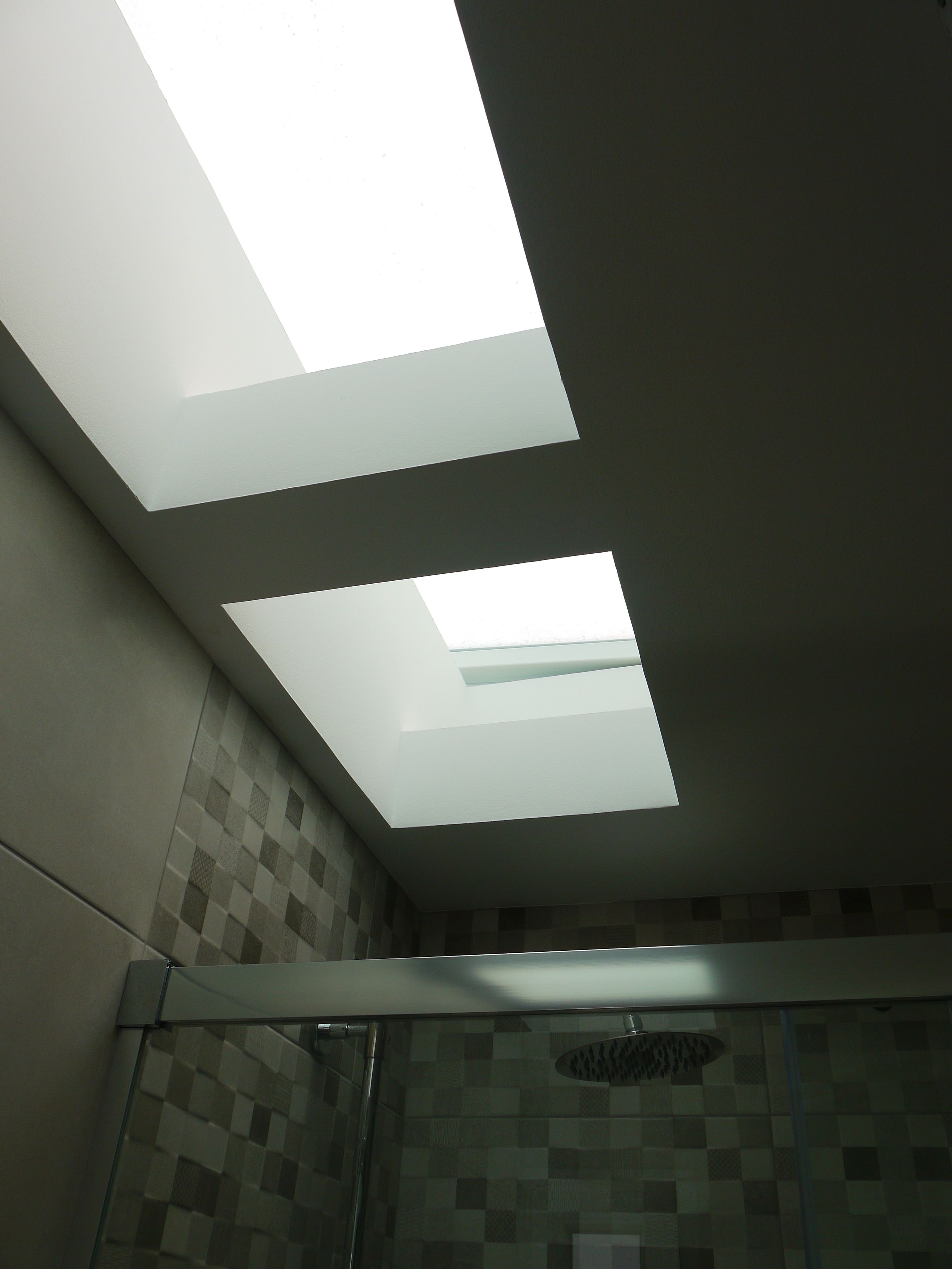 A bathroom with skylights, a shower, and a tiled wall.