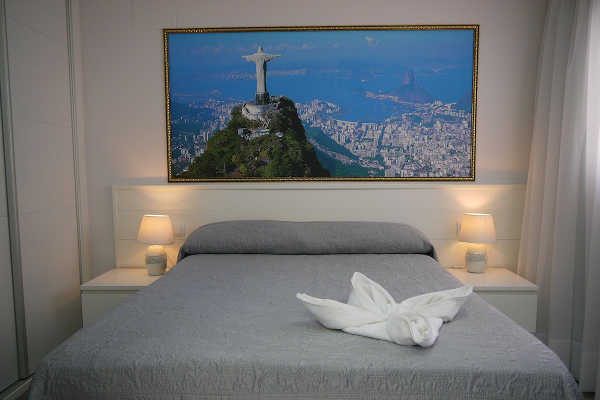 A hotel room with a bed, two bedside lamps, and a large framed picture of Christ the Redeemer on a mountain.