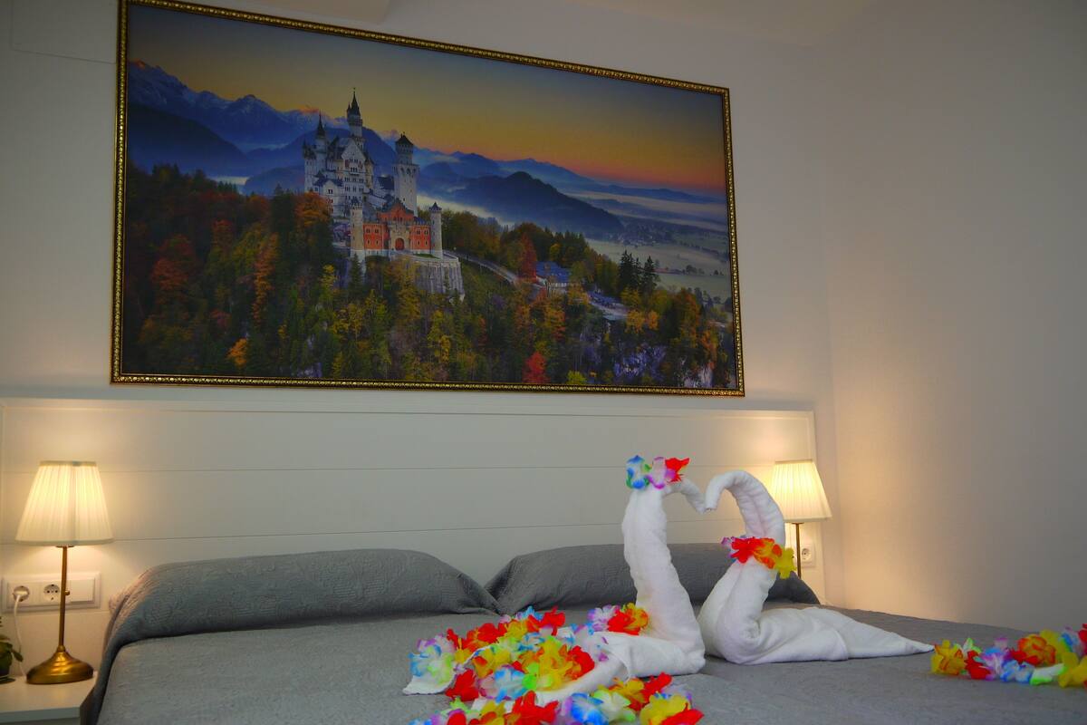 A hotel room with a bed, two bedside lamps, and a painting of a castle on the wall.
