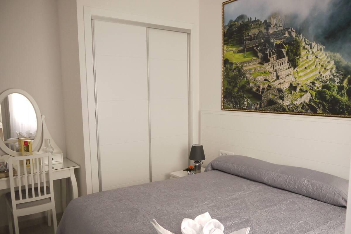 A bedroom with a bed, a bedside table with a lamp, a mirror, and a dresser.