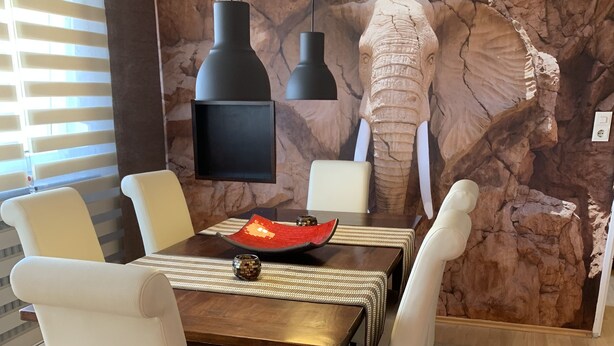 Comedor con mesa de madera, sillas blancas y un mural de pared de roca.