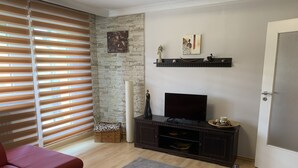 Una sala de estar con un sofá rojo, una mesa de centro de madera, un televisor sobre un mueble oscuro, una pared de piedra y una puerta.