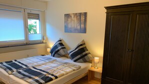 Un dormitorio con cama, mesita de noche, lámpara, armario y un cuadro en la pared.