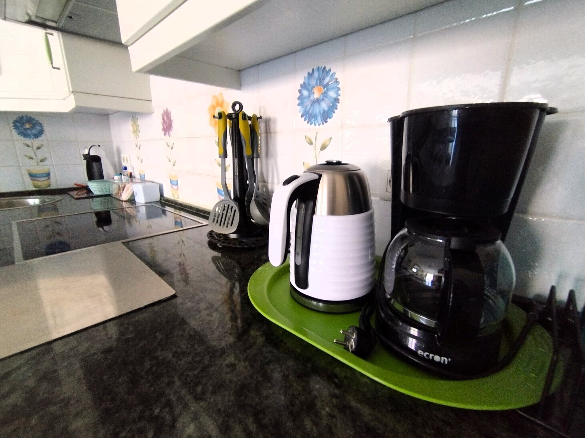 Une cuisine équipée d’une machine à café, d’une bouilloire et d’une spatule, le tout posé sur un plateau vert.