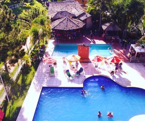 A pool area with multiple pools, lounge chairs, umbrellas, and a small building with a tiled roof. - Ecoresort Chales San Thomaz (Belmiro Braga)