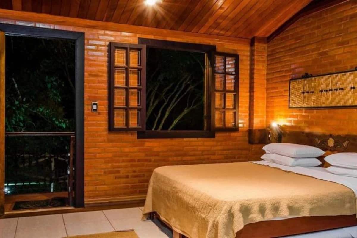 A wooden room with a bed, a window, and a wall-mounted light fixture.