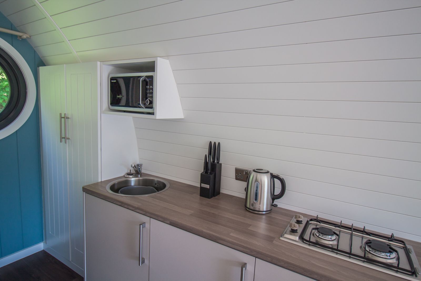 A compact kitchen with a sink, stove, and a microwave above the countertop.