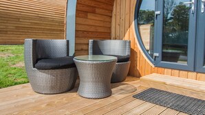 Een houten terras met twee rieten stoelen en een glazen tafel.