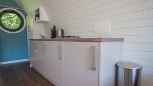 Een keuken met witte kasten, een roestvrijstalen prullenbak en een raam met uitzicht op bomen.