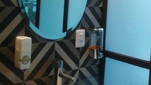Une salle de bain avec un mur orné d’un motif géométrique, un miroir rond, un lavabo blanc et un sèche-mains.