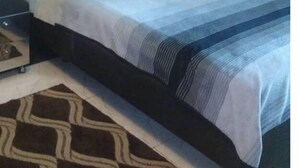 Une chambre à coucher avec un lit, un tableau représentant un paysage urbain accroché au mur et un tapis à motifs.