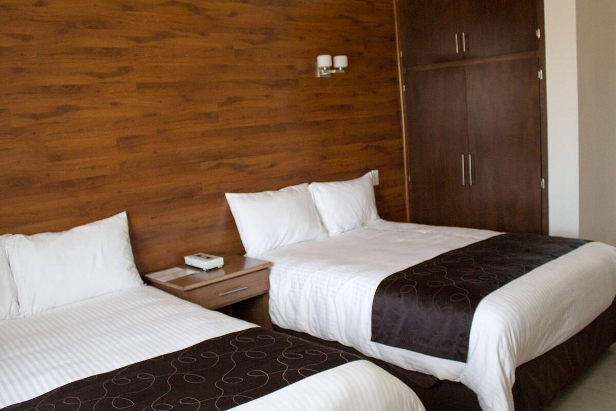 A hotel room with two beds, wooden headboard, nightstands, and a wardrobe.