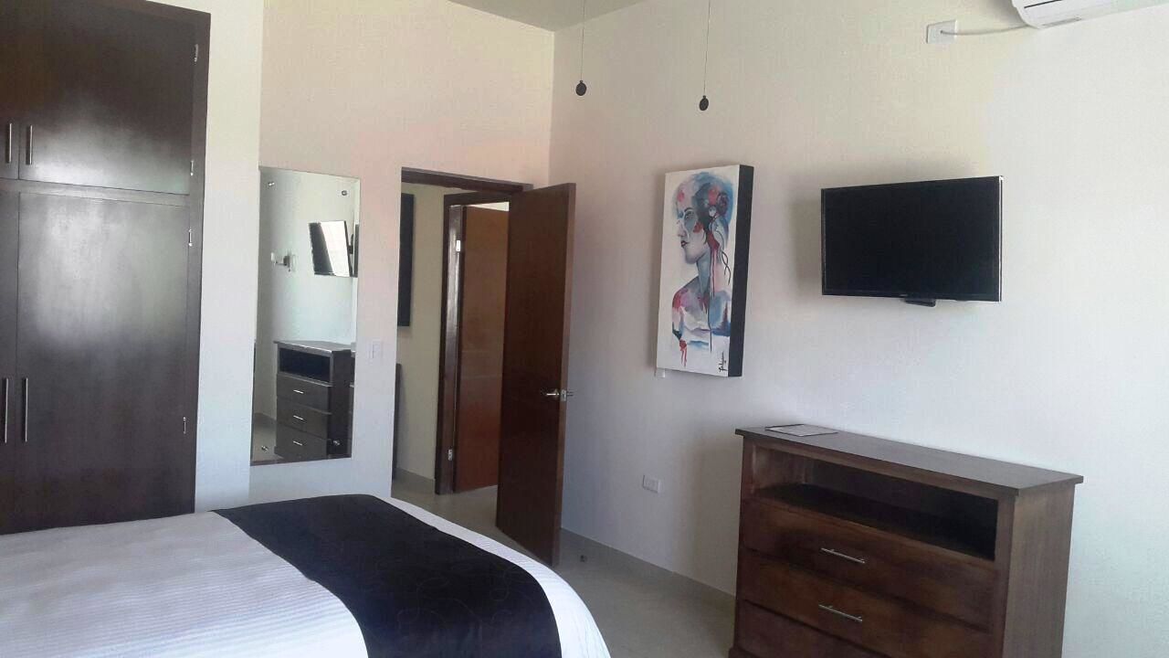 Een slaapkamer met een bed, een kledingkast, een televisie en een schilderij aan de muur.