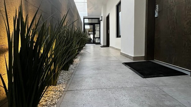 Un pasillo moderno con piso de concreto, barandilla de metal y una puerta a la derecha.