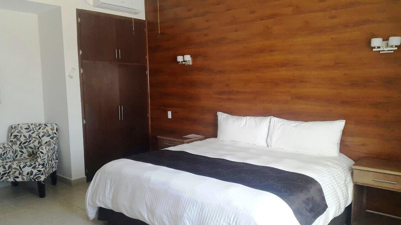 A bedroom with a bed, a wooden wardrobe, a chair, and a nightstand with a lamp.