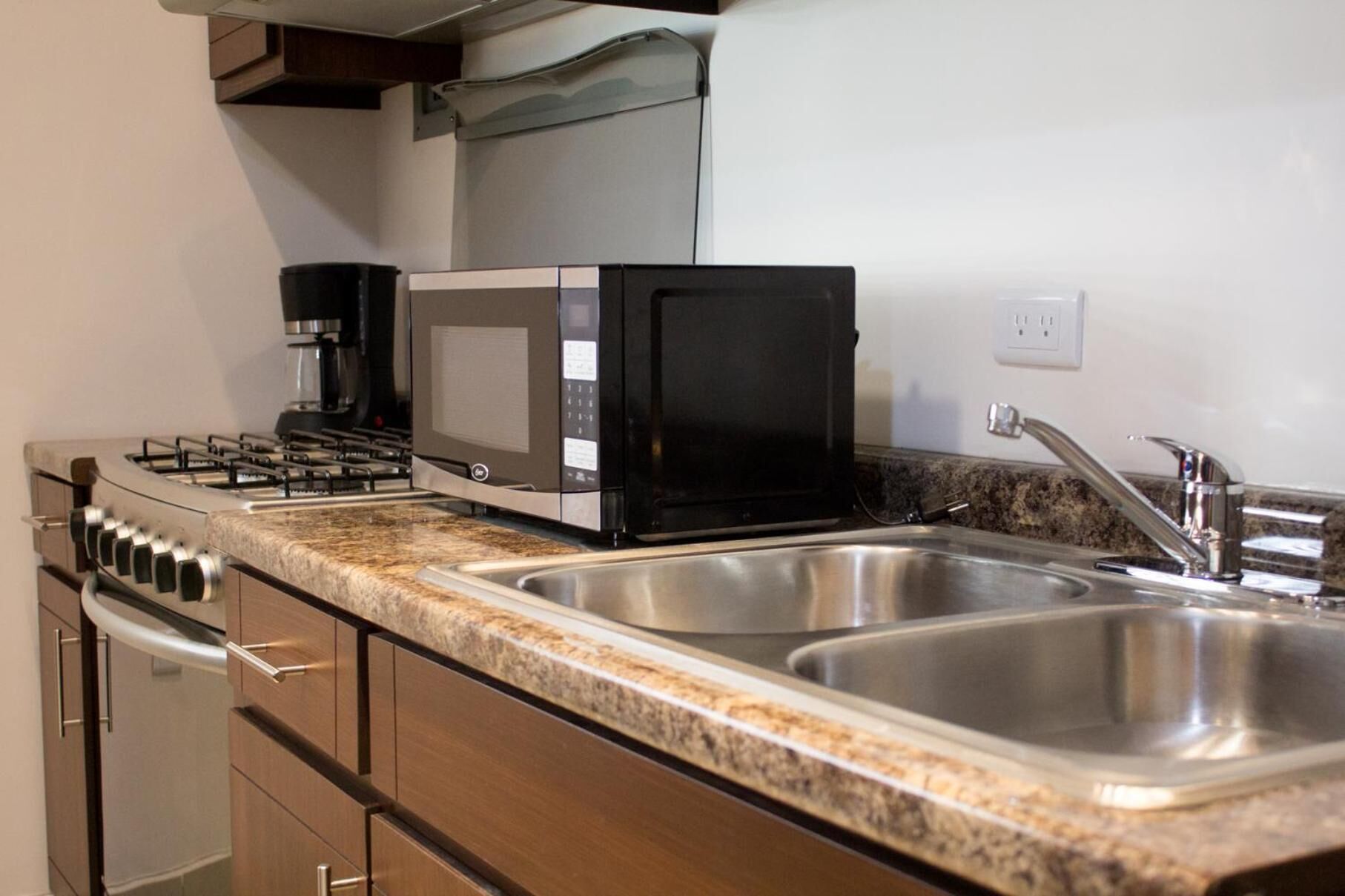 A kitchen with a gas stove, a microwave, and stainless steel sinks.