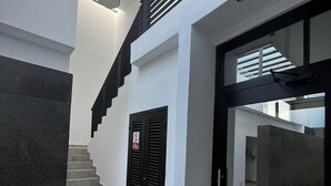 Un interior moderno con una escalera que sube a un segundo piso, una puerta de cristal y un pilar de piedra.