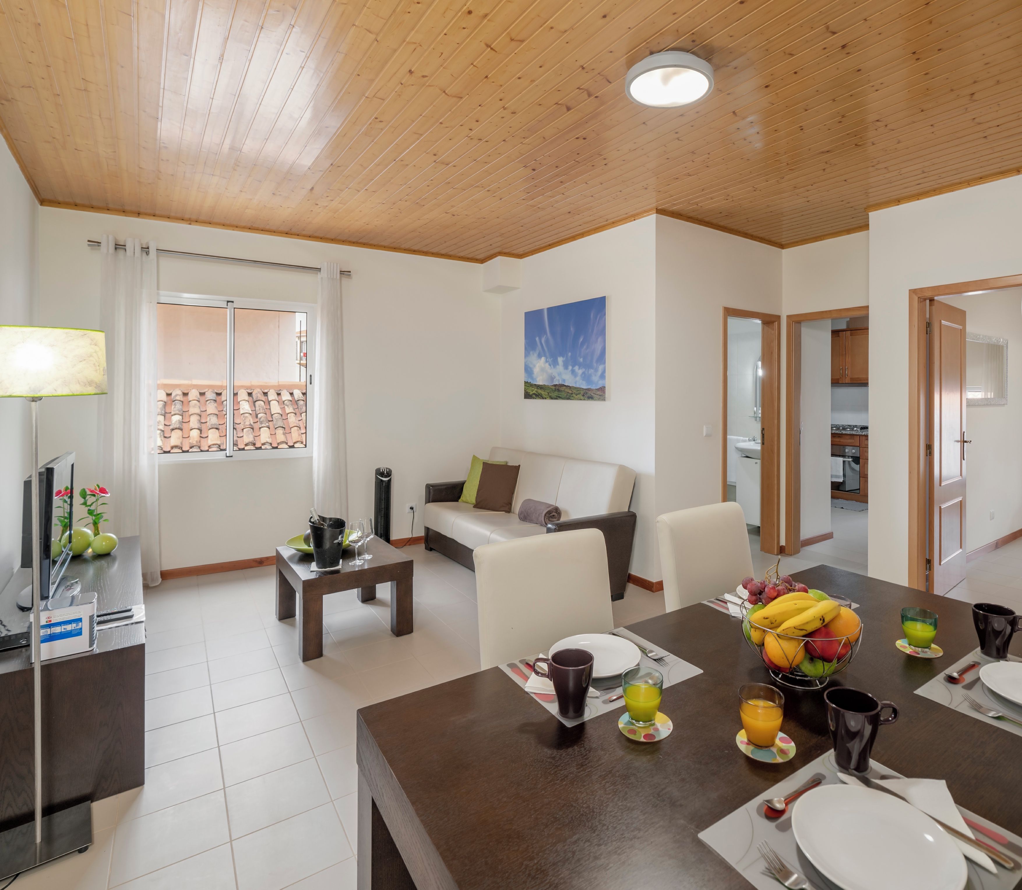 A modern living room with a dining area, wooden ceiling, and a "Clean & Safe" sign.