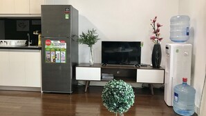 A modern kitchen with a refrigerator, a flat-screen TV, a water dispenser, and a potted plant.