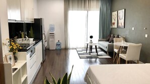A modern hotel room with a kitchenette, a sofa, a dining table, and a bed.