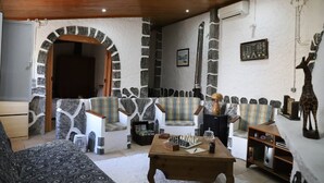 A cozy living room with stone walls, a wooden ceiling, and a fireplace. There are two armchairs and a sofa. A chessboard is on a wooden table. - Refúgio Saloio in Lousa-LRS (Lousa)